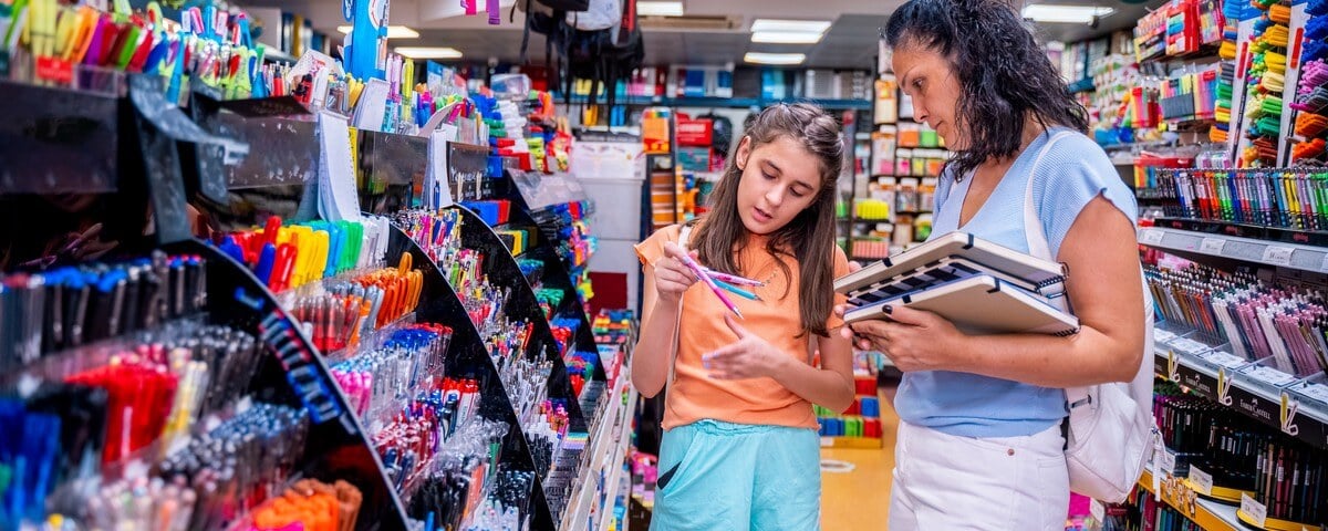 Une mère et sa fille font l'épicerie dans un magasin ; l'enfant essaie de choisir quel crayon acheter.
