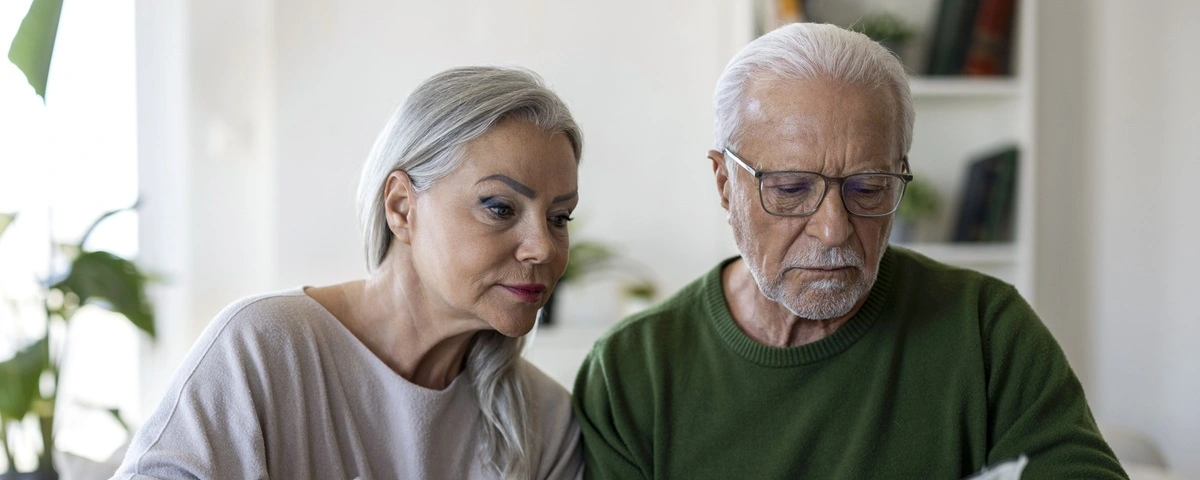 Un couple de personnes âgées assis à une table chez eux, en train de passer en revue des factures et des reçus à l'aide d'une calculatrice, de gérer ensemble les dépenses du foyer, de établir un budget et de gérer leurs finances personnelles.