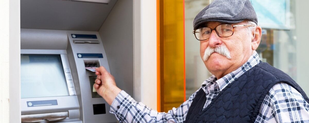 Un homme âgé insérant sa carte de crédit dans un guichet automatique à l'extérieur
