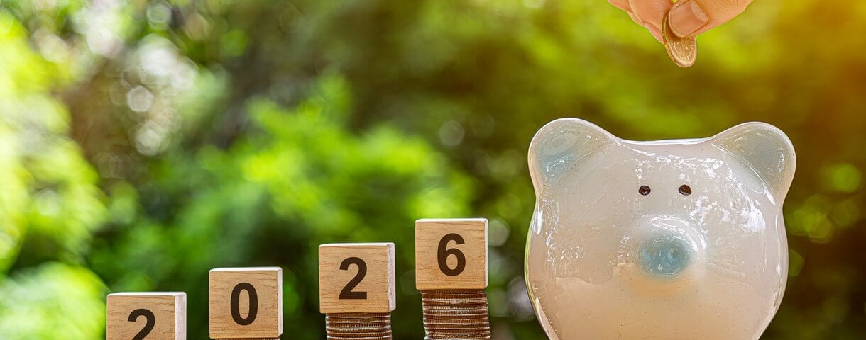Des pièces de monnaie empilées avec des cubes en bois portant l'année 2026 sur un fond naturel. Tirelire. Le Nouvel An 2026 est placé sous le signe des finances et de l'épargne.