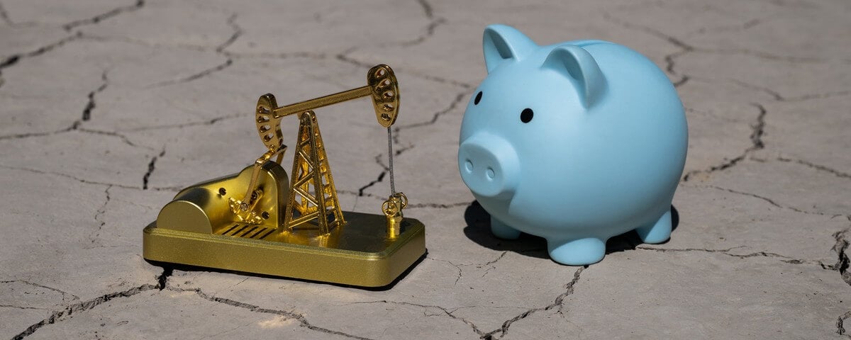 Une pompe à pétrole miniature en or et une tirelire posées sur de l’argile fissurée dans le désert