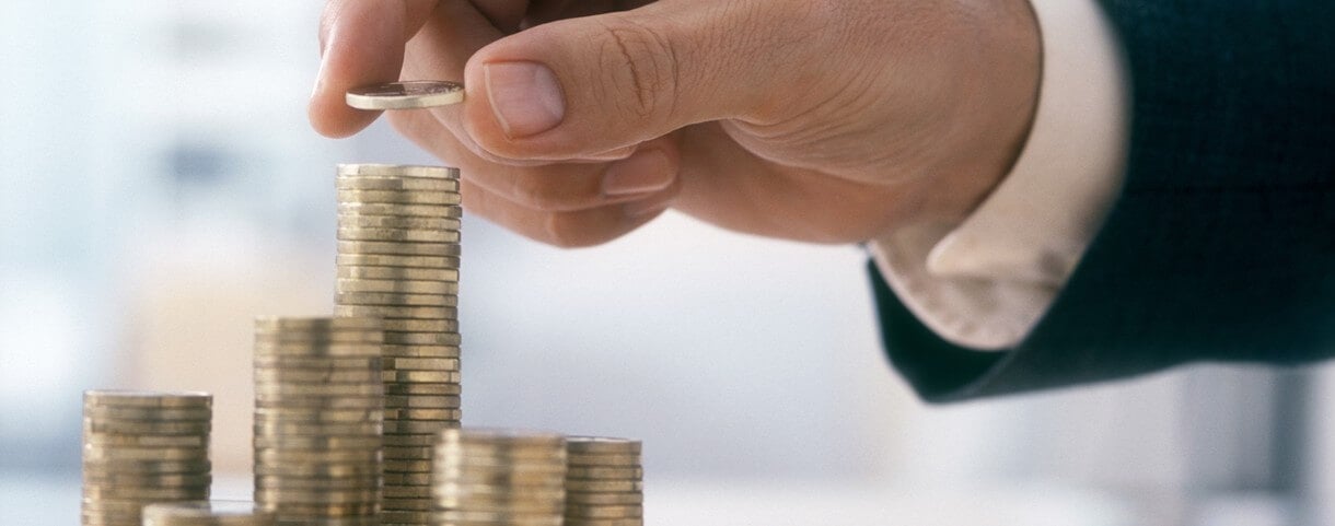 La main d'un homme d'âge mûr, vêtu d'un costume, empile des pièces en euros.